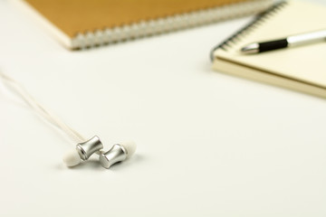 earphone with diary book and pen on white desk background.