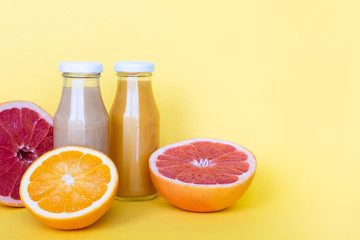 Raw fruit juices in glass bottles on yellow background. Healthy concept. Copy space