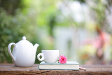 White coffee cup and kettle with notebooks on wooden table with pink rose