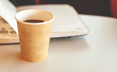 Coffee in a recyclable paper disposable glass with an open notebook in background