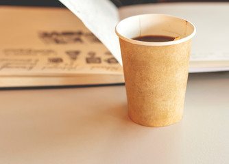 Coffee in a recyclable paper disposable glass with an open notebook in background
