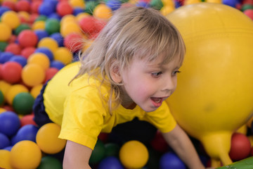 Fototapeta na wymiar Portrait of a blond boy in a yellow t-shirt. The child smiles and plays in the children's playroom. Ball pool.