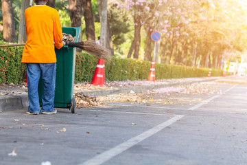 Asian man worker cleaning the road with green trash bin.