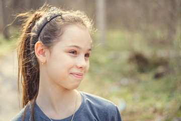 Cute smiling teenage girl standing outdoors Portrait of smiling girl looking at camera on background of spring tree in daylight