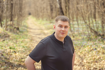 A young male among the trees. Portrait of a young attractive man standing  in autumnal park covered with foliage in daytime