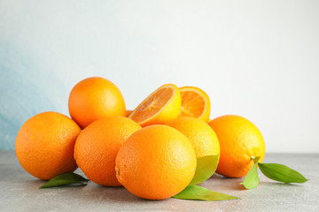 Ripe oranges with leaves on grey table against light background, space for text