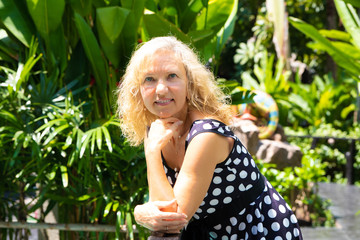 portrait of a 50-year-old woman in summer against a background of green tropical palm trees.