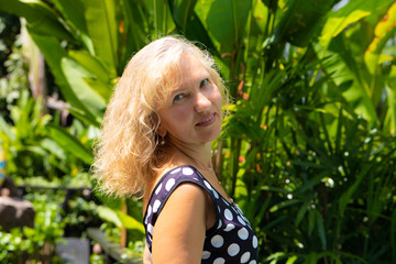 portrait of a 50-year-old woman in summer against a background of green tropical palm trees.