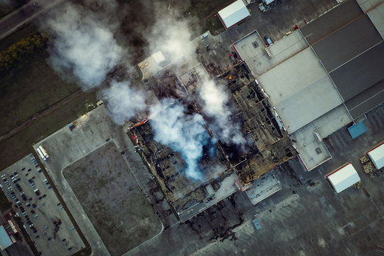 Top down view of smoke clouds from burnt warehouse building with burned roof, fire disaster accident in cargo logistics storehouse, aerial shot