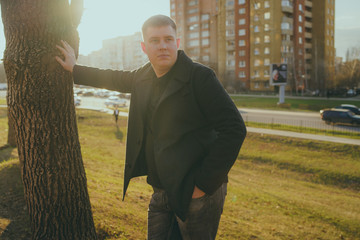 Man standing beside trees in sunny day Portrait of young man in casual clothes posing among trees...