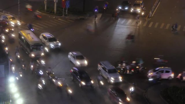 Close Up Front Overhead View Of Night Timelapse View Of Cars, Buses, Motorcycles, And Scooters Circling Around A Traffic Circle In Saigon, Ho Chi Minh City, Vietnam.