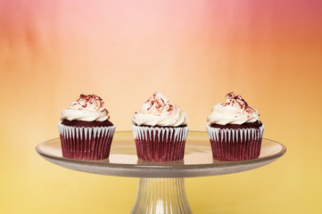 three frosted cupcakes on a cake stand with a bright colorful background