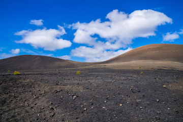 Spain, Lanzarote, Black volcanic mountains covered by some green plants under blue sky