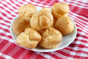 Homemade small cakes profiterole choux pastry with custard next to a white cup with tea and books on a table with a rustic tablecloth in a red-white cage
