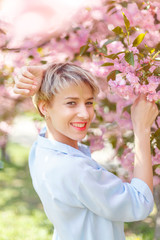 Fototapeta premium Young attractive blonde girl posing near a blossoming cherry tree. Spring mood.