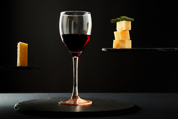 Portion of red wine and pieces of cheese on black background