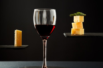 Portion of red wine and pieces of cheese on black background