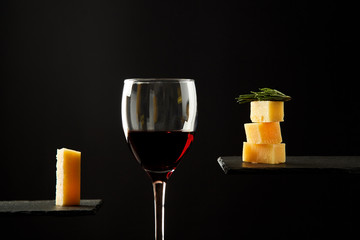 Glass of red wine and pieces of cheese on black background