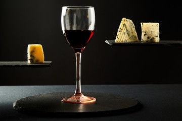 Glass of red wine and pieces of cheese on black background