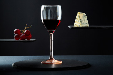 Composition of red wine in glass beside blue cheese and grape on black background