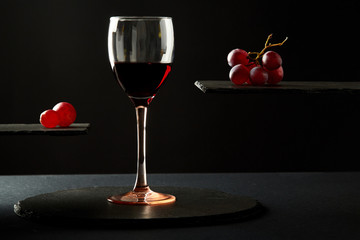 Sweet red wine in glass and fresh grape berries on black background