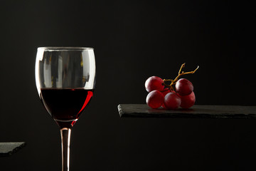 Sweet red wine in glass and fresh grape berries on black background