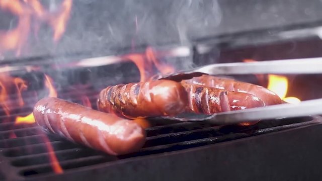 juicy pork sausages are fried on a hot grill in the fire. Turn the tongs. Close up. slow motion