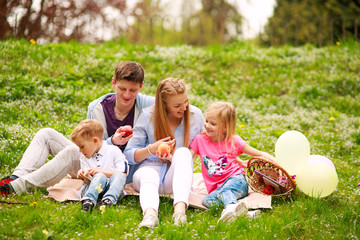 Fototapeta premium Happy family on picnic in flowered park sitting on grass, parenthood leisure in nature