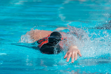 Freestyle swimmer in black swim cap moving towards the camera.  Bright, sunny afternoon.  Light blue water splashing.