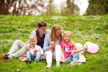 Naklejka na ściany i meble Happy family on picnic in flowered park sitting on grass, parenthood leisure in nature