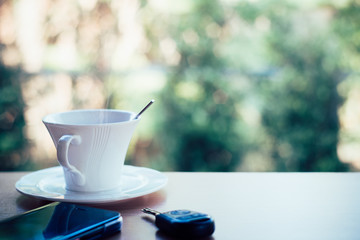 Cup of hot coffee , Key and smartphone in cafe
