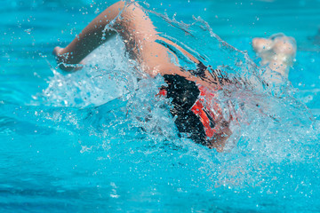 Freestyle swimmer in black swim cap moving towards the camera.  Bright, sunny afternoon.  Light blue water splashing.