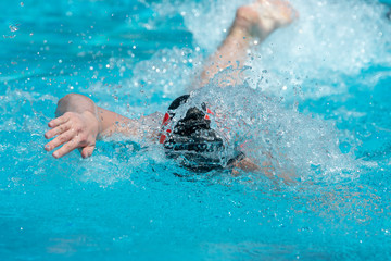 Freestyle swimmer in black swim cap moving towards the camera.  Bright, sunny afternoon.  Light blue water splashing.