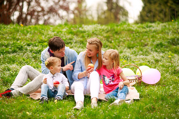 Fototapeta premium Happy family on picnic in flowered park sitting on grass, parenthood leisure in nature
