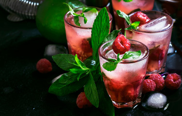 Alcoholic cocktail raspberry mojito with berry, lime, syrup, soda, rum, mint and crushed ice. Steel bar tools, black bar counter, selective focus