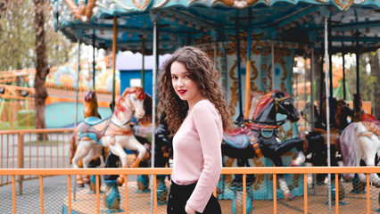 Fototapeta na wymiar Stylish young hipster woman posing outdoors on the background of carousels. Girl enjoys a summer day