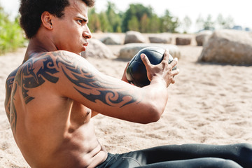 Muscular man exercise with medicine ball at the beach