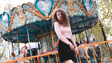 Obraz na płótnie Canvas Stylish young hipster woman posing outdoors on the background of carousels. Girl enjoys a summer day