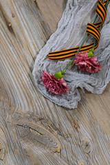 Two pink carnations, Saint George ribbon on a wooden surface.