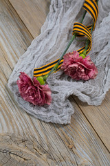 Two pink carnations, Saint George ribbon on a wooden surface.