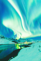 Aurora Borealis natural phenomenon on Lofoten Islands in Norway, Scandinavia, Europe. Night sky with northern lights over mountains and road reflected in fjord. Night winter landscape with aurora.