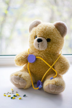 Cute teddy bear with a phonendoscope next to pills in the pediatric healthcare concept