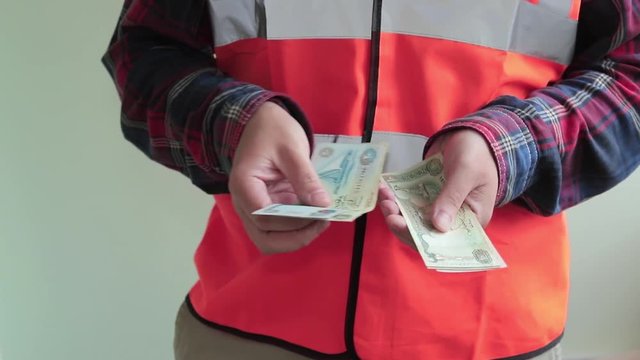 Man worker dressed in a reflective vest count arab bills dirhams and gives money to the camera.. Hands closeup isolated on light green background.