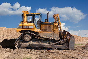 Yellow dozer on a dirt terrain with blue sky with clouds in the background