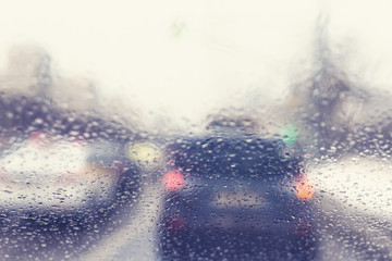 Blurred view through the windshield of a car with raindrops on the stop signals car. Concept of drive safety on the road and speed limit