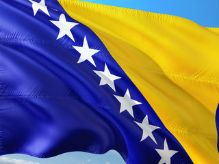 Flag of Bosnia and Herzegovina waving in the wind against deep blue sky. High quality fabric.