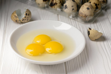 Close up a plate with yolks and whites of quail eggs and a plastic container with eggs in the background