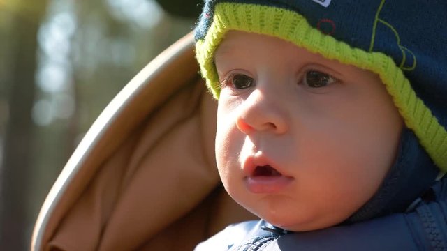 Little one year old baby boy sits in perambulator and looks around