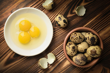 Top view yolks and whites of quail eggs in a plate and a bowl filled with eggs on a wooden table