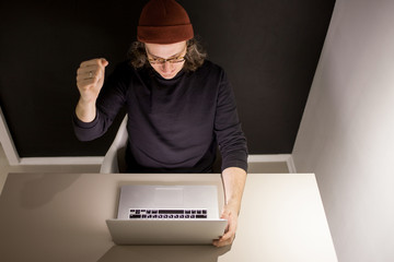 Designer or programmer in the workplace. young man in a hat and glasses sitting at a laptop.